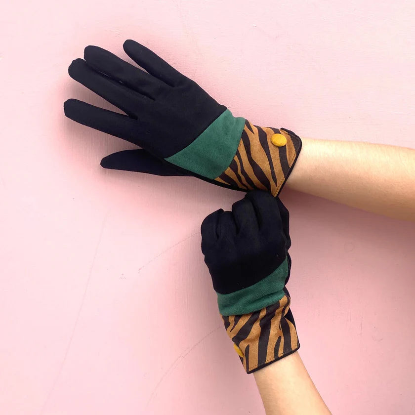 Black and teal suedette gloves with tiger print wrist detail and yellow button, shown on hands against a pink background.