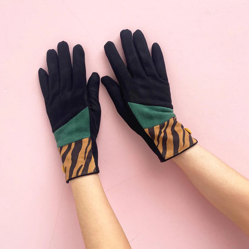 Pair of animal print tiger suedette gloves with teal and black panels, displayed flat on arms against a pastel pink backdrop.