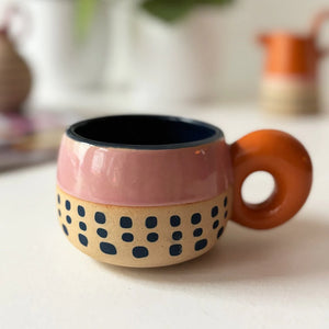 Bloc Cup with pink glaze, navy dotted base, and orange circular handle on a white surface.