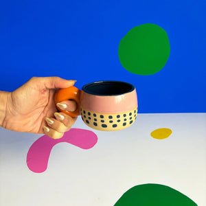 Bloc Cup held in hand, showcasing terracotta loop handle and hand-painted design on pink and beige ceramic.