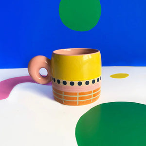 Bloc Mug with yellow glaze and pink doughnut handle on abstract background.