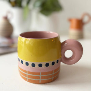 Bloc Mug on white surface with yellow and pink glaze, navy dot pattern, and circular handle.