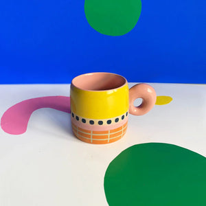 Colourful Bloc Mug featuring yellow glaze, grid design, and pink handle on graphic backdrop.