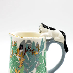 Close-up of the black and white ceramic cat perched on the jug handle, highlighting gold detailing and leaf illustrations.