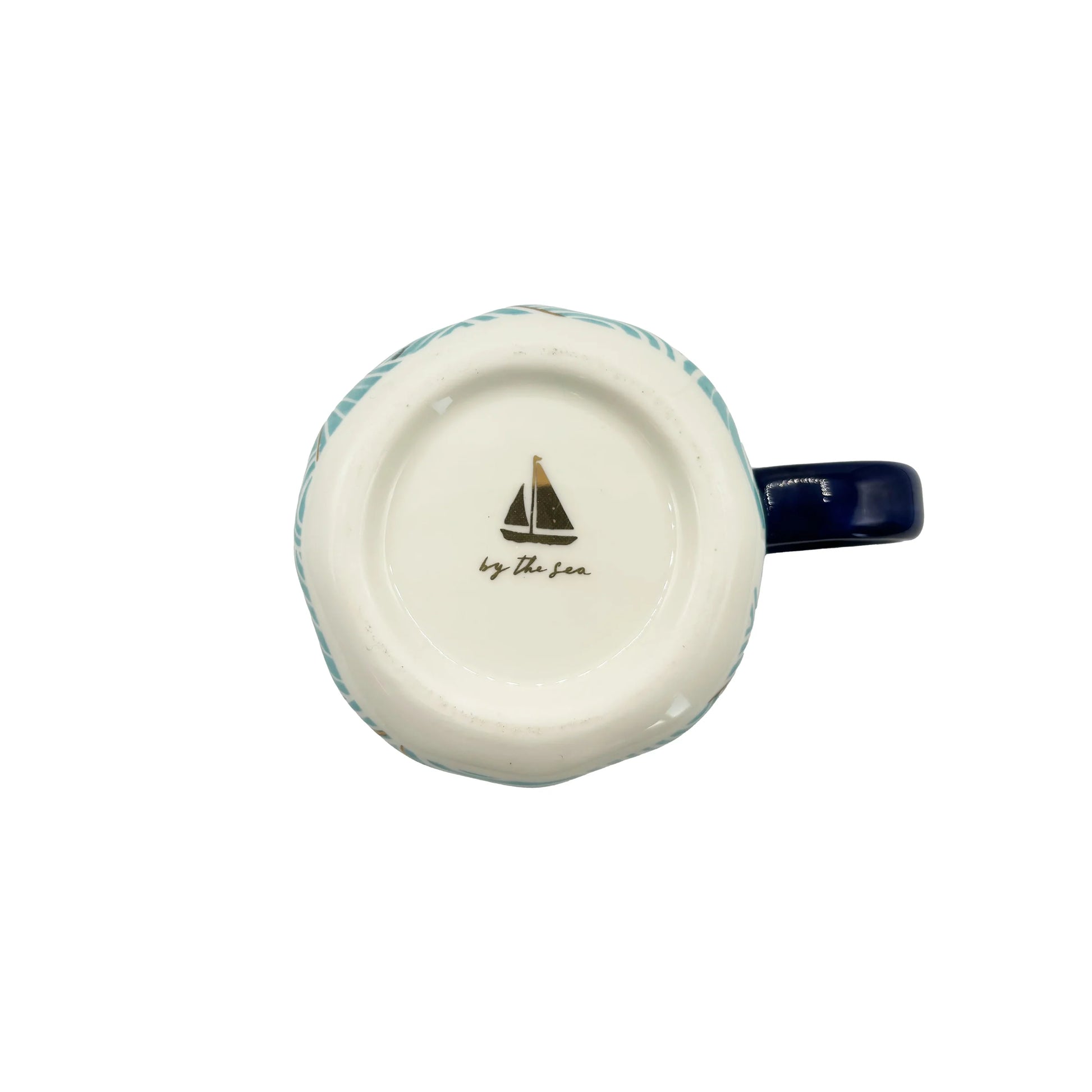 Base of ceramic mug showing sailboat illustration and “by the sea” text.
