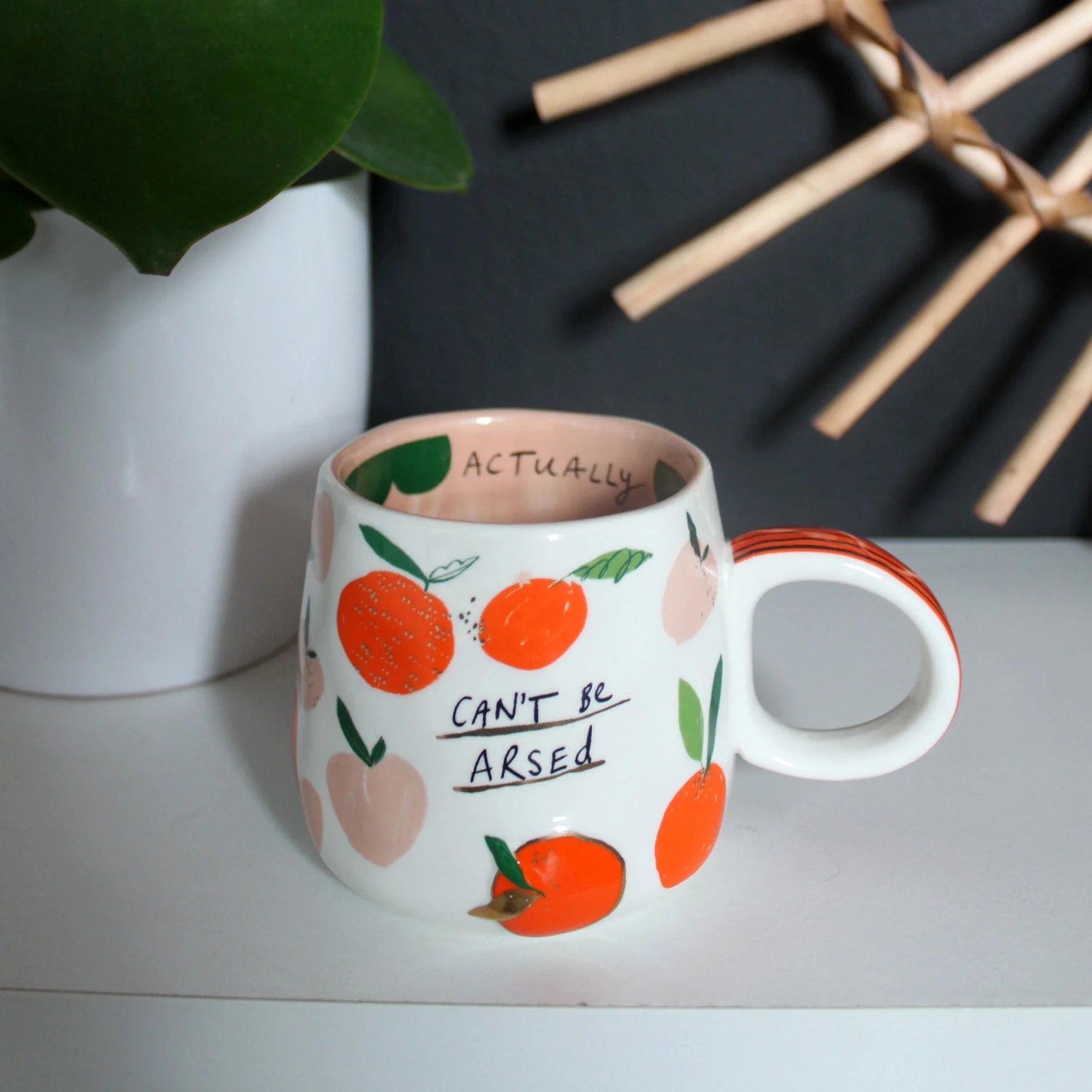 Funny handmade-style mug with orange and peach design, sitting on a shelf with the hidden message “Actually” visible inside the rim.
