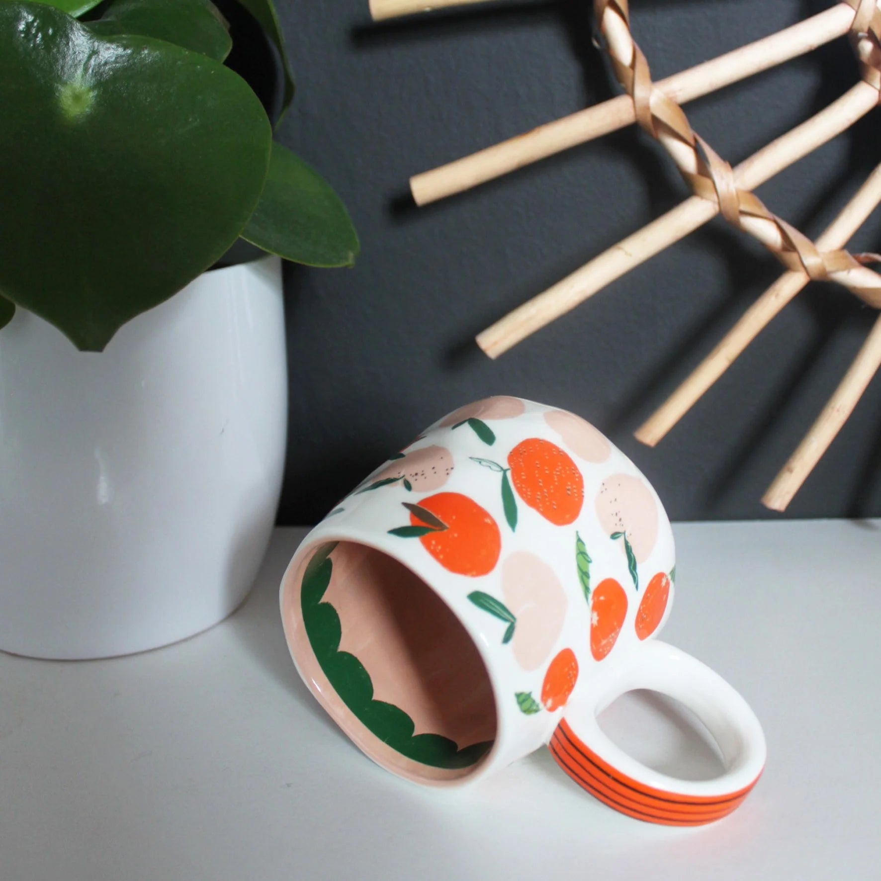 “Can’t Be Arsed” mug tipped on its side to show interior peach-pink glaze and green scalloped detail, surrounded by peach fruit illustrations.