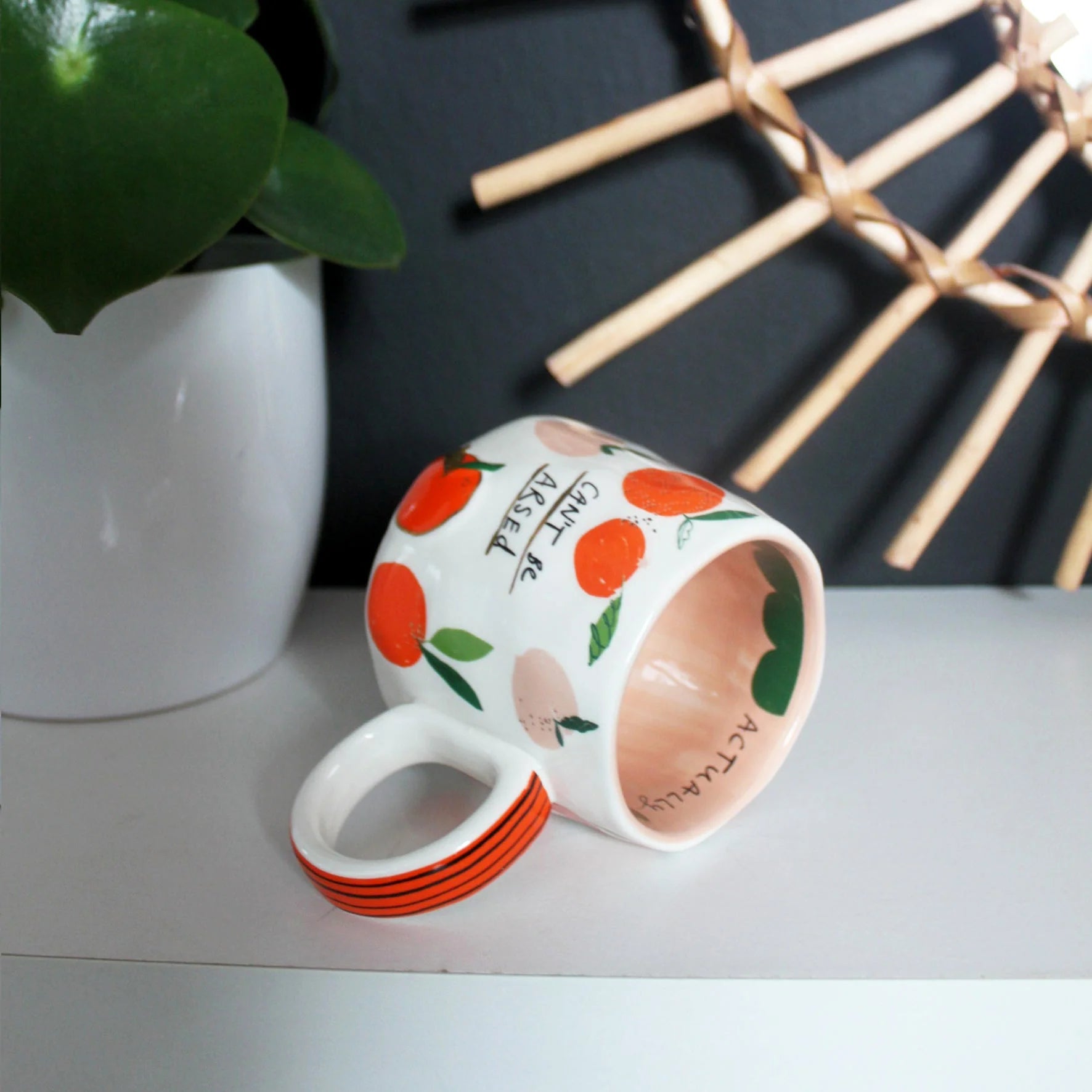 Ceramic mug with bold peach print and humorous text, lying on its side with orange striped handle and inner decal reading “Actually”.