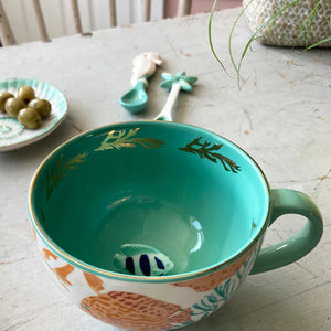 Close-up of the inside of the Coral Fish Mug revealing a 3D ceramic fish figurine at the bottom of the cup, surrounded by turquoise glaze.