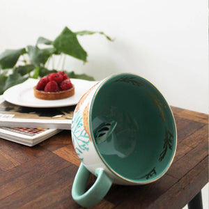 Coral Fish Mug tipped on its side to showcase the inner ceramic fish detail and golden coral illustrations along the rim.