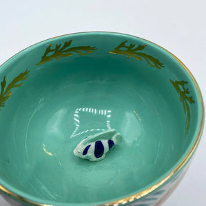 Top-down view of Coral Fish Mug with turquoise glaze and miniature ceramic fish detail at the base, highlighted by reflective lighting.
