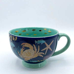 Front view of Coral Lobster Cup showcasing navy exterior with a crab, starfish, and marine illustrations in gold and pastel tones.