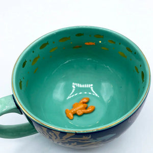 Top-down view into Coral Lobster Cup, revealing the glossy turquoise glaze, goldfish detailing, and small orange ceramic lobster inside.