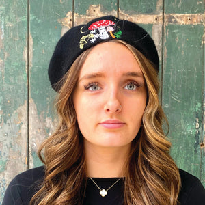 Model facing forward wearing black Forage beret with colourful mushroom and foliage embroidery – fairycore style winter accessory.
