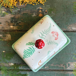 Overhead view of the woodland-themed butter dish on a rustic wooden table, showing whimsical mushroom and foliage pattern in full.