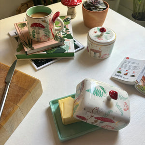 Butter dish in use with lid lifted to reveal butter inside, styled on a white table with matching mug and jar from the Forage collection.