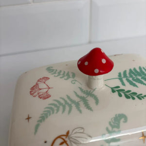 Close-up of the toadstool-shaped knob on the butter dish lid, showing glossy red finish and delicate leaf and flower designs on the porcelain surface.