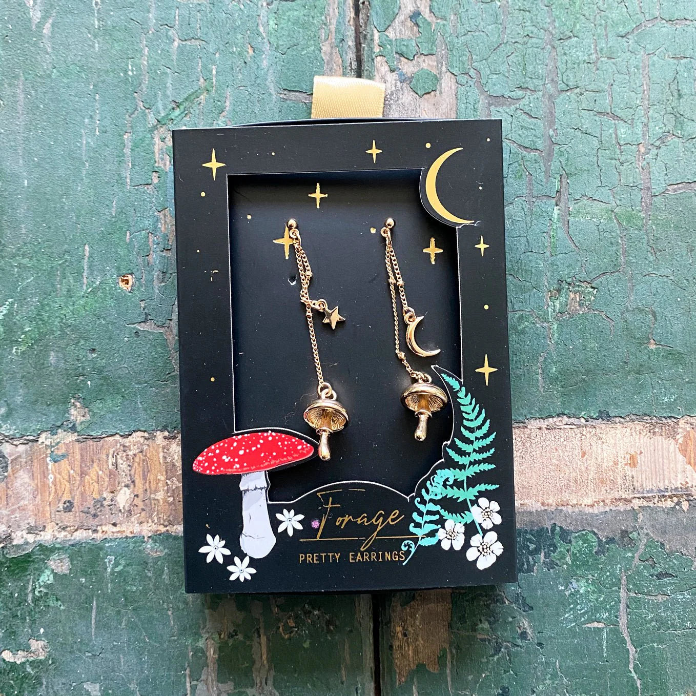 Forage Gold Earrings in illustrated black gift box featuring a red toadstool, ferns, stars, and gold foil moon detail on the packaging.
