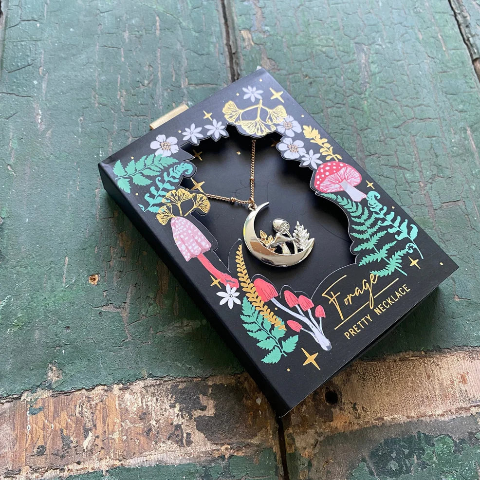 Forage Moon Necklace displayed in its illustrated gift box with gold foil botanical artwork, showing the crescent moon pendant with mushroom and foliage design.