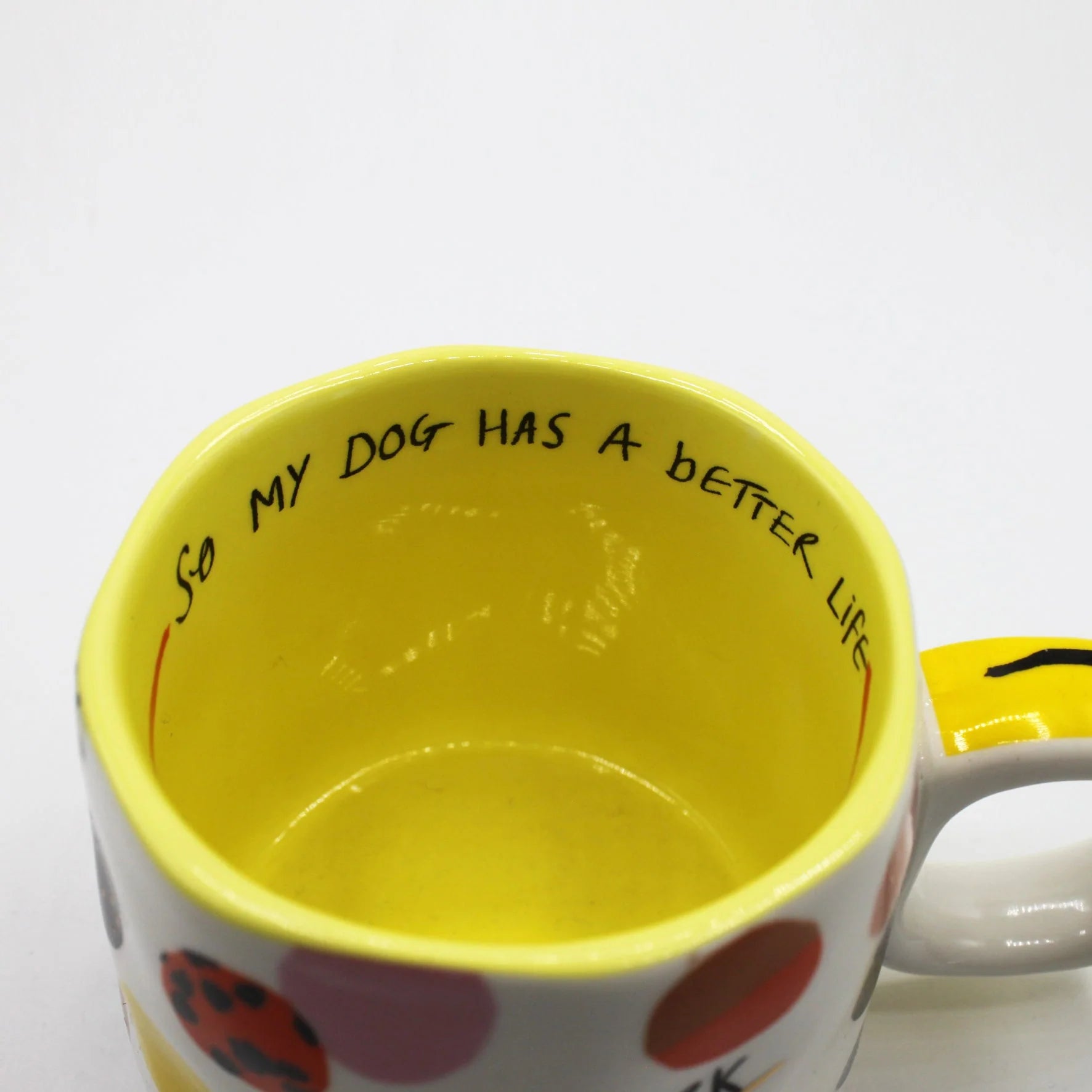 Close-up of yellow-glazed interior with handwritten message “So my dog has a better life” inside rim of ceramic mug.