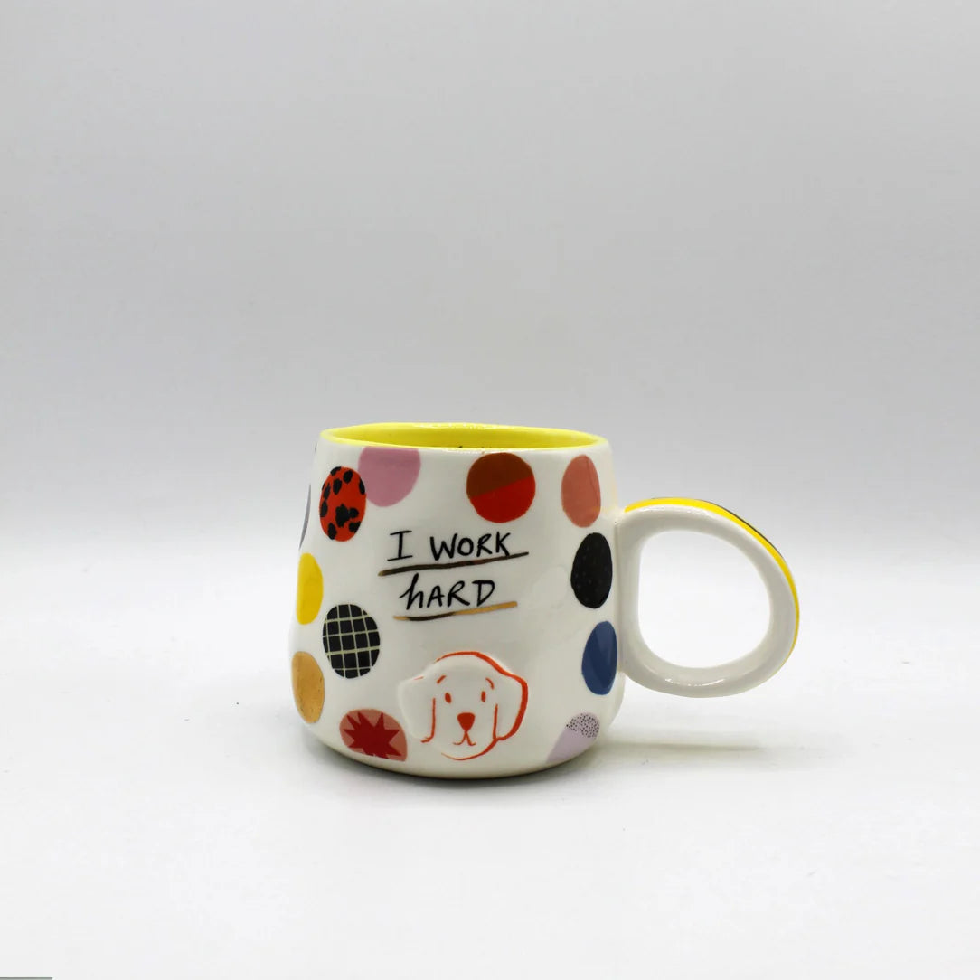 Front-facing view of ceramic mug with colourful spots, 3D dog face, and bold “I work hard” lettering.
