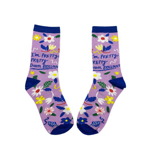 Pair of “I’m Pretty Damn Brilliant” socks laid flat showing slogan on both and multicoloured flowers throughout.