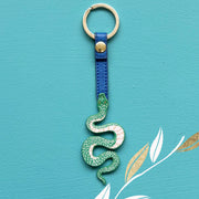 Front view of Inked Snake Keyring with coiled green tattoo-style snake and blue vegan leather strap against turquoise background.