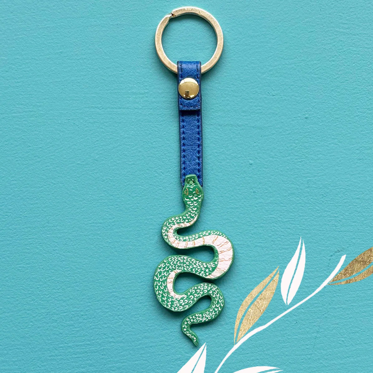 Front view of Inked Snake Keyring with coiled green tattoo-style snake and blue vegan leather strap against turquoise background.