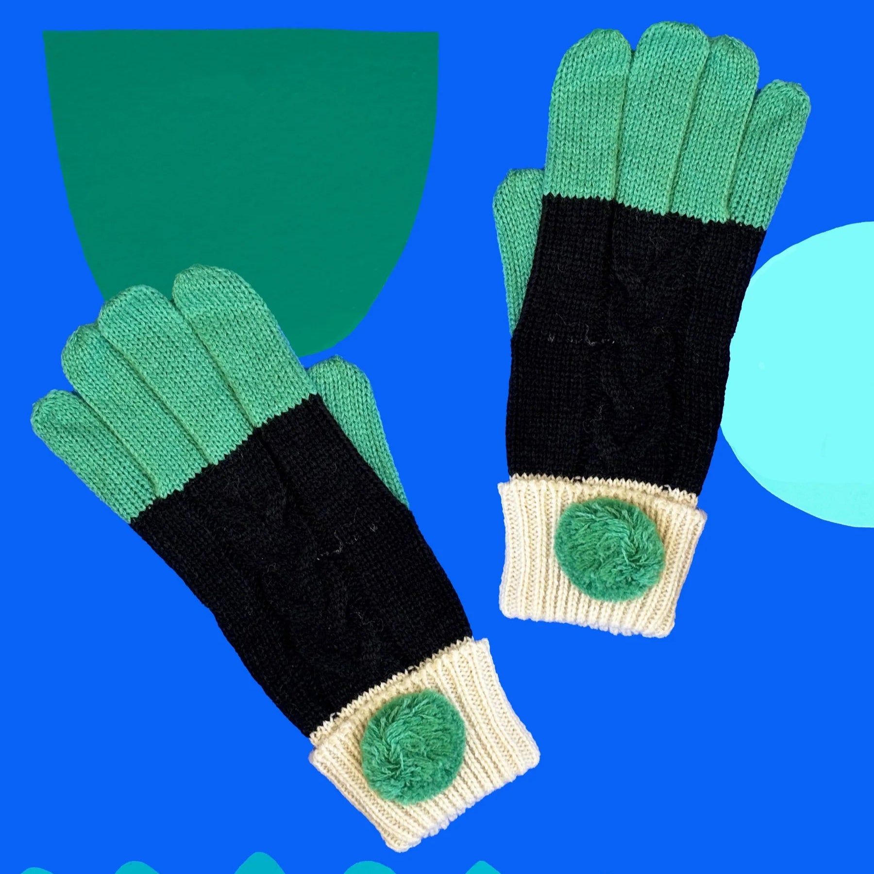 Pair of Loop Black Gloves with mint green fingers, black knit body, and cream cuffs with mint pom-poms on a bright blue background.