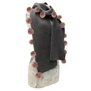 Charcoal grey cable knit scarf with peach and blue pom poms styled on mannequin bust.