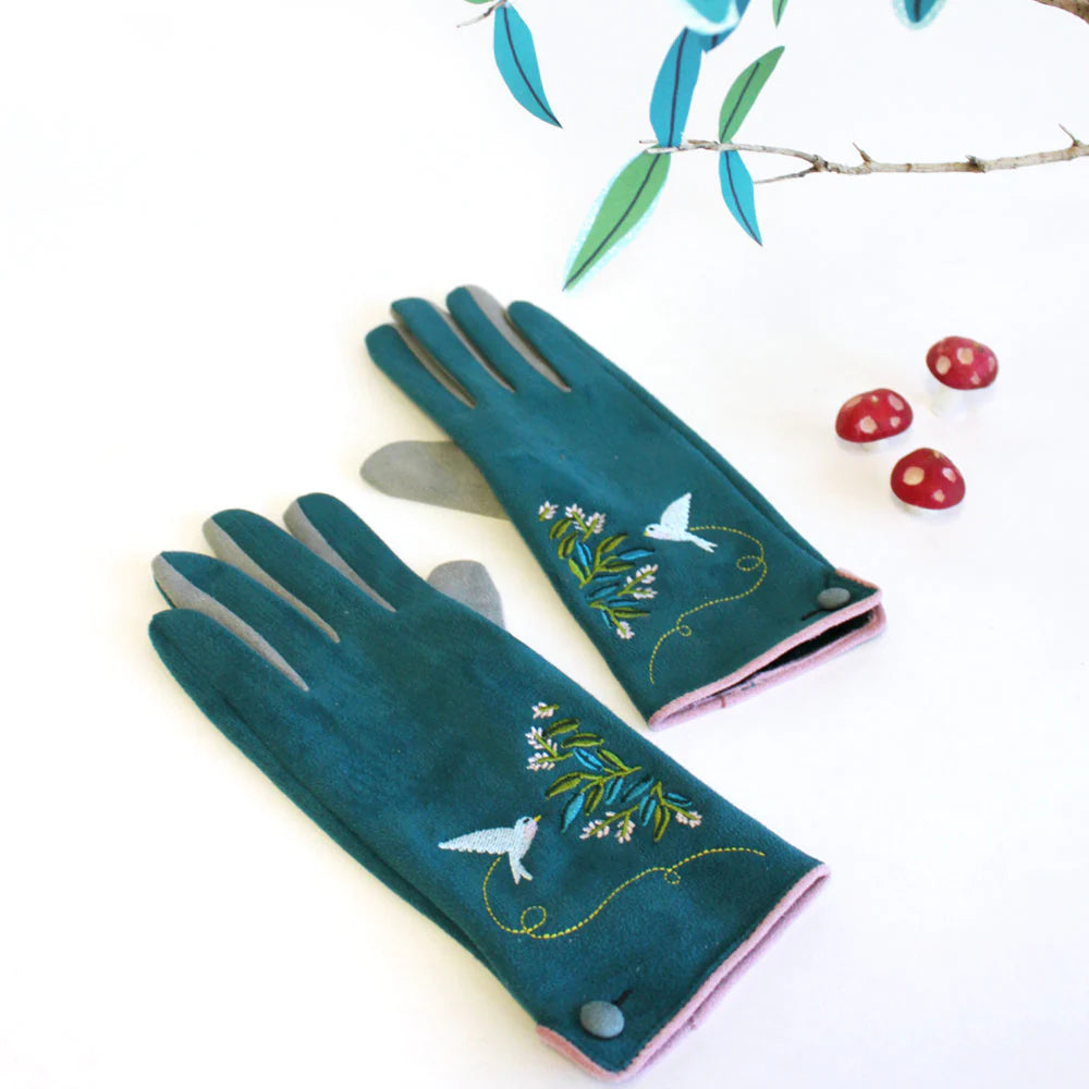 Flat lay of teal fashion gloves with bird and floral embroidery, styled with faux mushrooms and paper leaves.