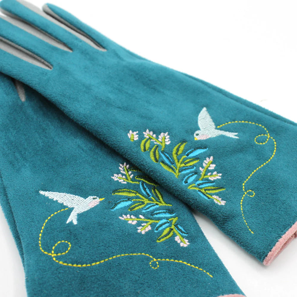 Close-up of teal embroidered gloves highlighting white bird and green leaf detailing with pink cuff trim.