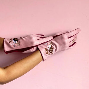 Model wearing deep blue gloves with embroidered hedgehogs and forest foliage on a soft pink background.