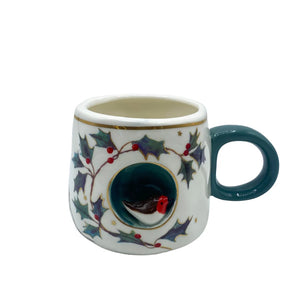 Studio shot of porcelain robin mug with green handle, holly leaf illustration, and sculpted robin inside.