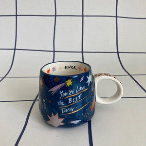 House of Disaster celestial ceramic mug with “You’re like the best thing” quote and star print, shown on gridded backdrop.