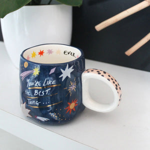 Blue starry mug with pink polka-dot handle and interior EVER message, styled in home setting.