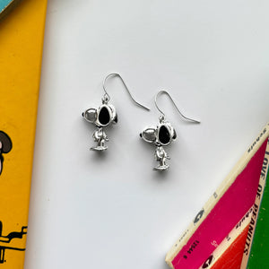 Close-up of Snoopy earrings on a white surface with vintage Peanuts books in the background.