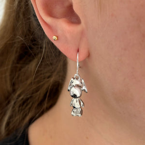 Snoopy earring worn by a model, showing its silver and black enamel details.