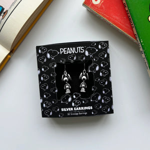 Snoopy earrings in black Peanuts-themed packaging, displayed with vintage Peanuts books.