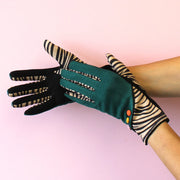 Pair of zebra animal print gloves with forest green fabric and colourful button detail, displayed on hands.