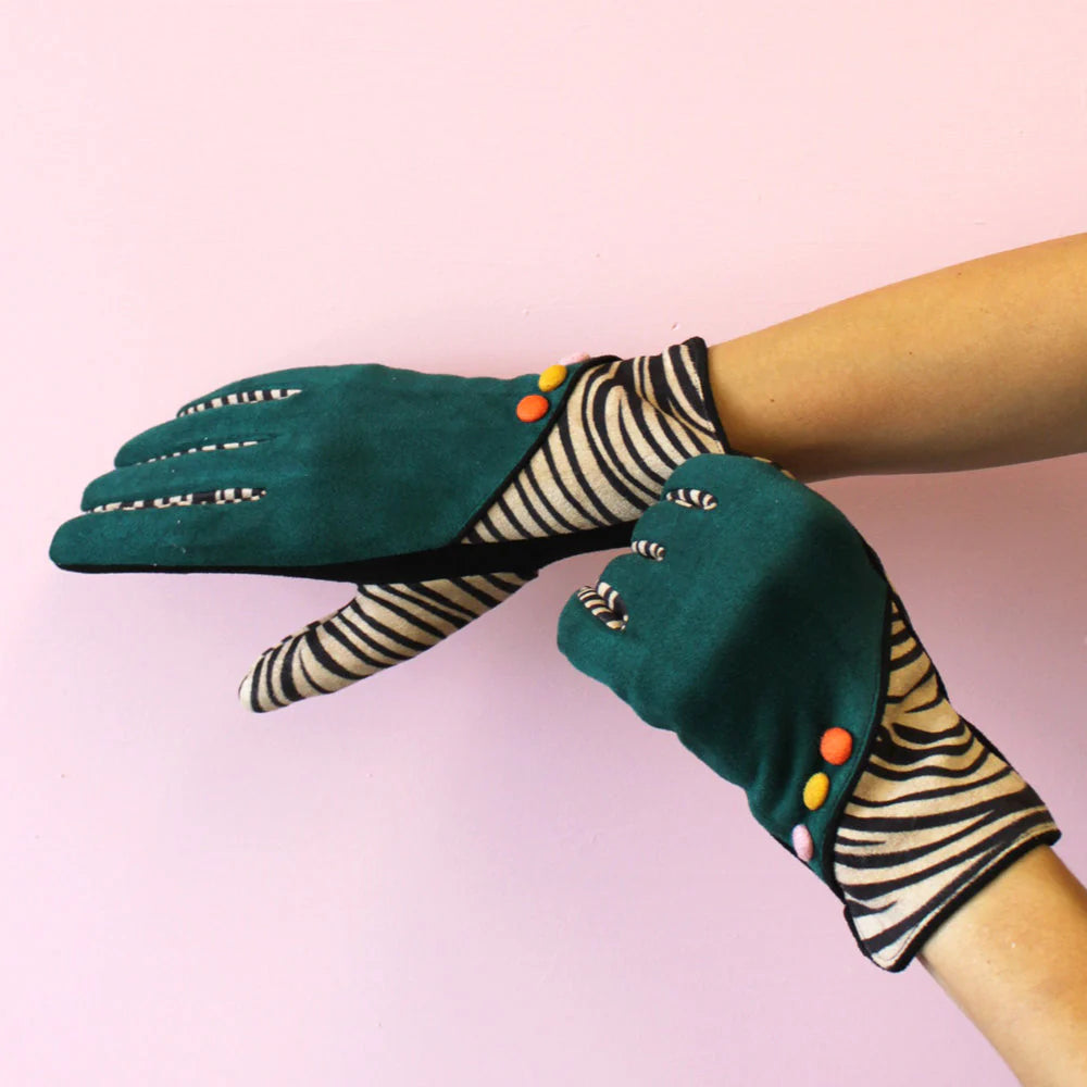Fashion gloves in forest green with zebra print cuffs and multicolour buttons, styled on hands against a pink background.
