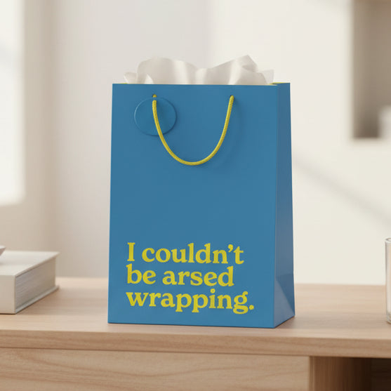 Teal blue slogan gift bag on wooden surface with tissue paper visible.
