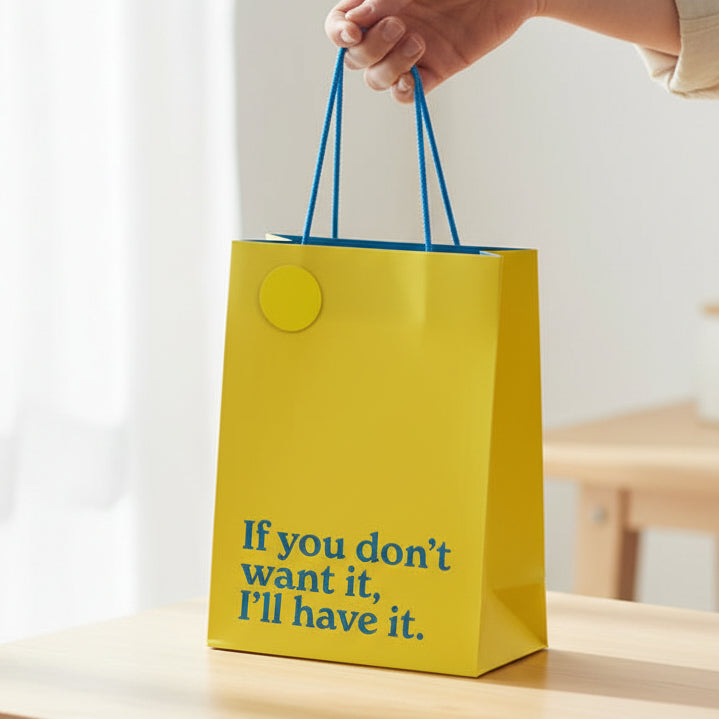 Yellow slogan gift bag held in hand showing teal text and rope handles.