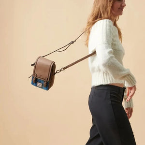 A woman walking outdoors, carrying a small, brown Harris Tweed bag with a leather handle. The bag is trailing behind her.