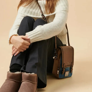 A woman sitting on a carpeted floor, with a small, brown Harris Tweed bag resting beside her.