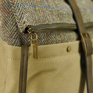 A close-up of a brown Islander Harris tweed canvas backpack in a chestnut herringbone pattern. A zipped pocket is visible on the front.