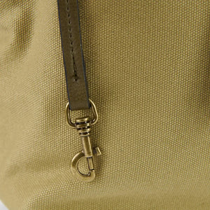 A close-up of a brown leather bag clip with a metal clasp, attached to a brown Islander Harris tweed canvas backpack.