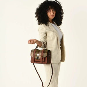 A Lady wearing the Islander Harris Tweed Chestnut Tartan Satchel from the strap with the shoulder strap hanging loose. 