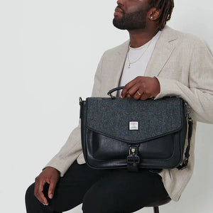 A man holding a black herringbone Harris Tweed laptop, showcasing its unique design and texture.