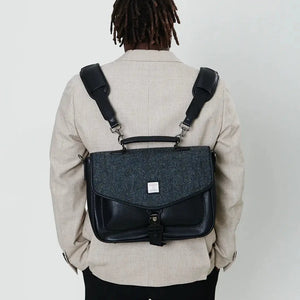 A man wearing a black herringbone Harris Tweed laptop case on his back, showcasing its convenient and stylish design.